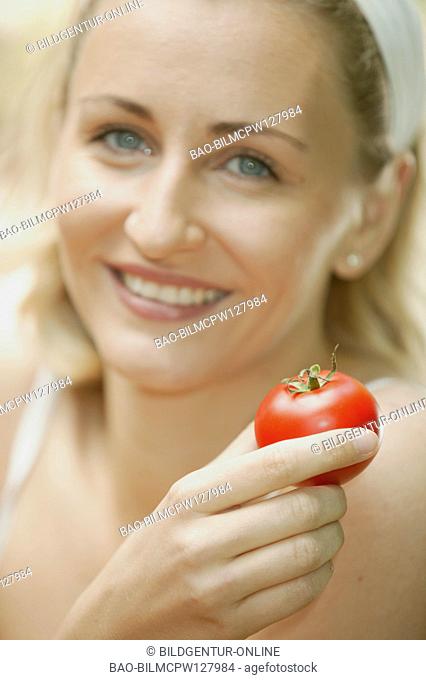 Woman shows a tomato in the garden, portrait
