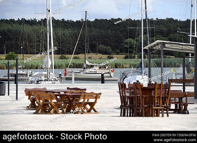 07 July 2020, Mecklenburg-Western Pomerania, Usedom: View over tables, chairs and benches to boats in the harbour of the town Usedom