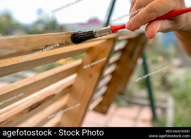 Hand of man painting wooden bench