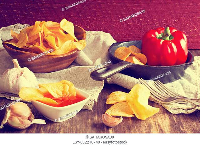 Potato chips and chili sauce on an old wooden table. Unhealthy food. Selective focus. Tinted image