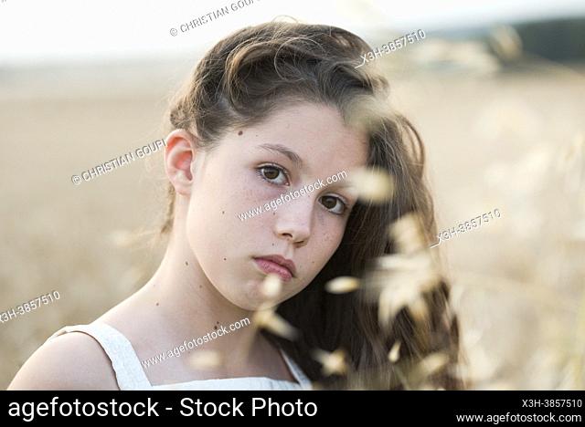 Girl in white dress on a path lined with cereal fields at sunset, France, Europe