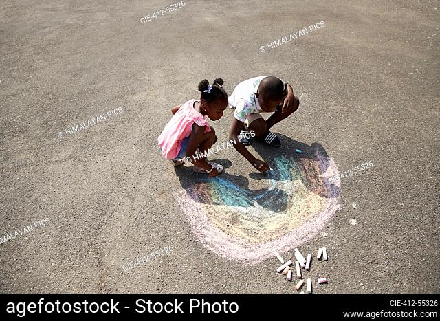Brother and sister drawing rainbow with sidewalk chalk on pavement