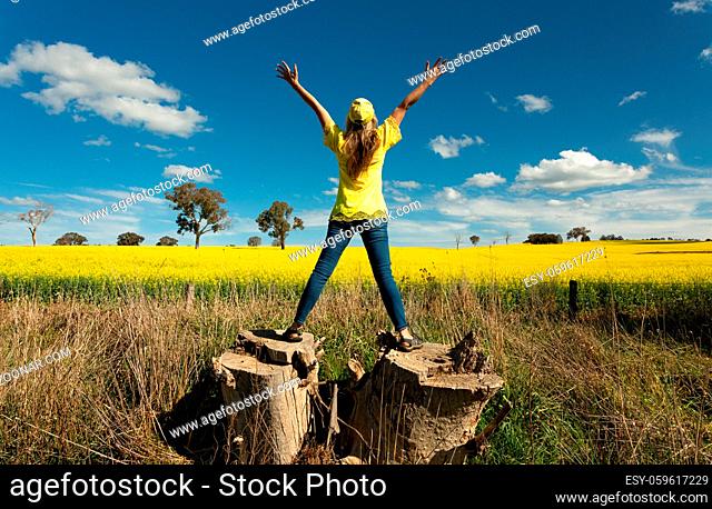 Woman enjoys the countryside views standing on large tree stump to view the canola fields in flower during spring