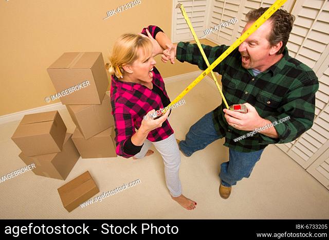 Couple having a fun sword fight with their tape measures surrounded by packed moving boxes