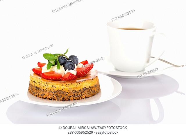 Cheesecake with strawberry, blueberry, mint and cream on white plate with cup of coffee and spoon