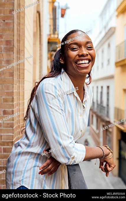 Cheerful woman leaning on railing in balcony