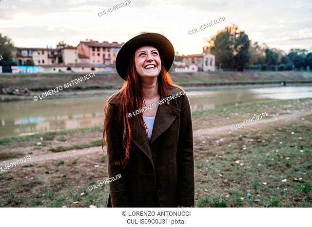 Young woman with long red hair laughing on riverside, Florence, Tuscany, Italy
