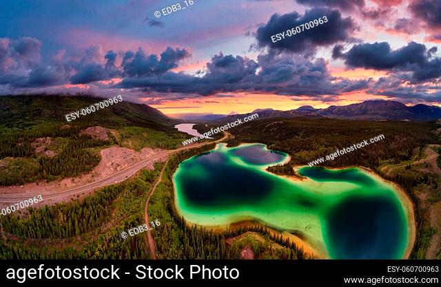 Panoramic View of Lakes from Above surrounded by Forest, alongside Scenic Road. Dramatic Sunset Sky. Aerial Drone Shot taken in Canadian Nature