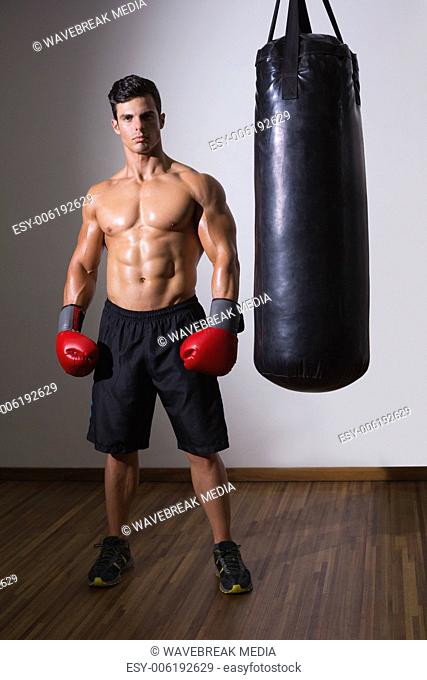Shirtless muscular boxer with punching bag in gym