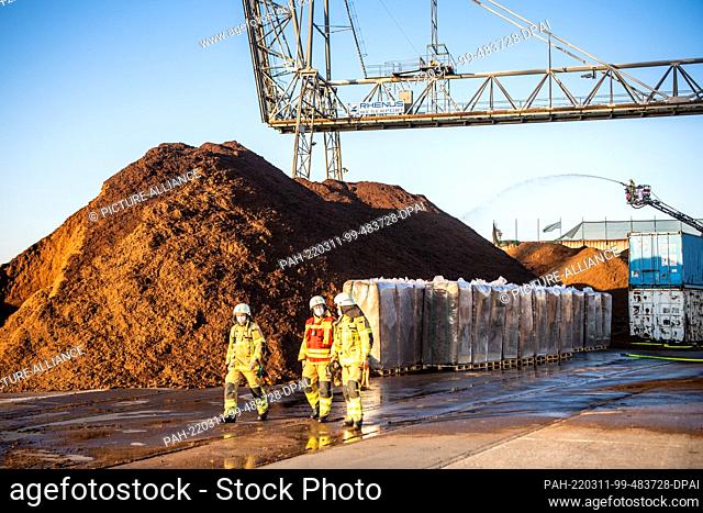 11 March 2022, Bremen: Firefighters walk through the industrial ports, where a large pile of peat caught fire. Residents of the surrounding areas were asked to...
