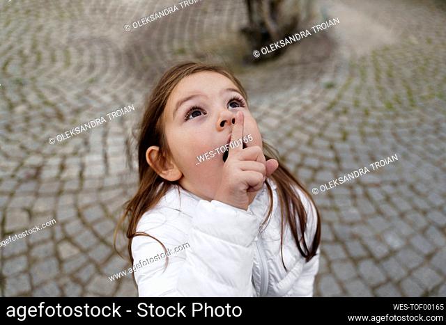 Cute girl with finger on lips looking up