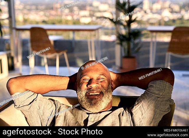 Smiling mature man relaxing on sofa at building terrace during sunset