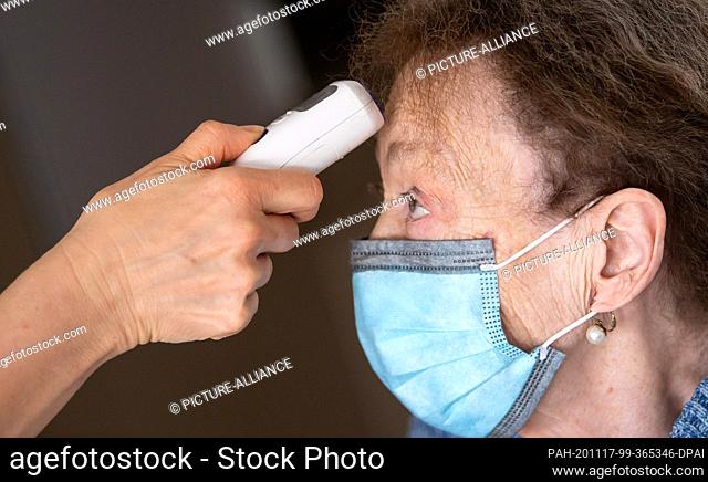 17 November 2020, Bavaria, Krailling: A nurse at the Maria Eich nursing home measures the temperature of a resident wearing a mouth and nose protector with a...