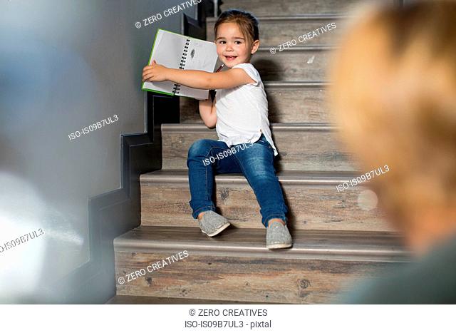 Girl on stairs proudly showing mother pencil drawings