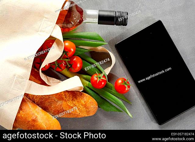 Tablet with fresh groceries and bottle of wine in a reusable textile carrier bag to save on pollution from plastics in the environment