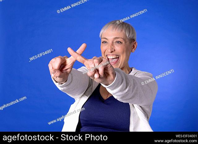 Happy woman making cross sign with fingers against blue background
