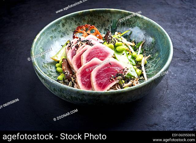 Modern style traditional Japanese gourmet seared tuna fish steak tataki with soba noodles and stir-fried vegetables served as close-up on a Nordic design bowl...
