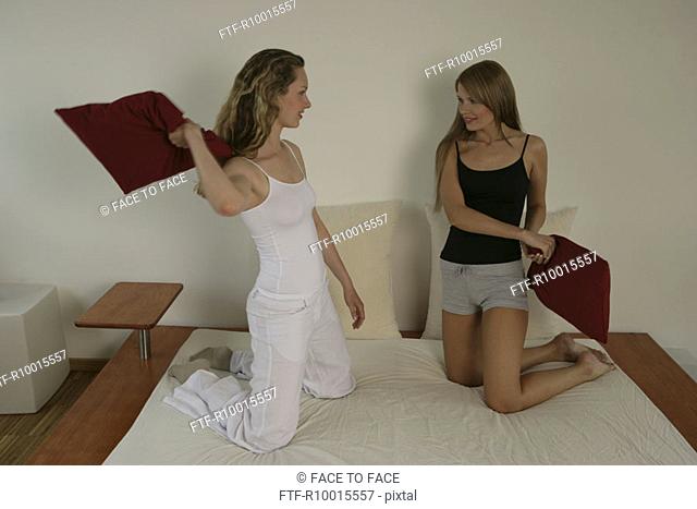 Two blonde women fighting with pillows on the bed