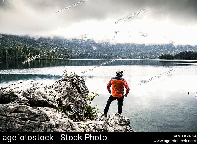 Man with hands on hip standing on rock by lake