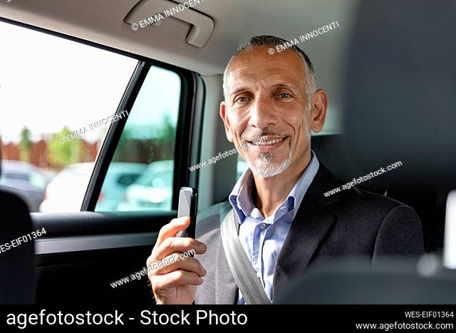 Male business professional holding smart phone while sitting in car