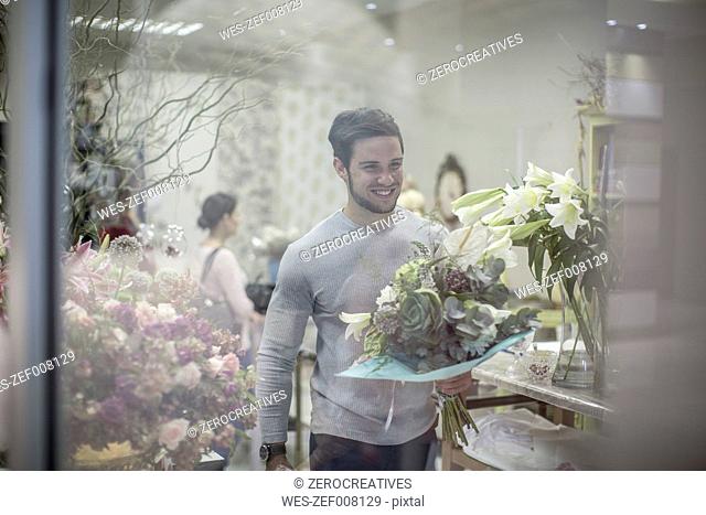 Smiling young man with bunch of flowers leaving flower shop
