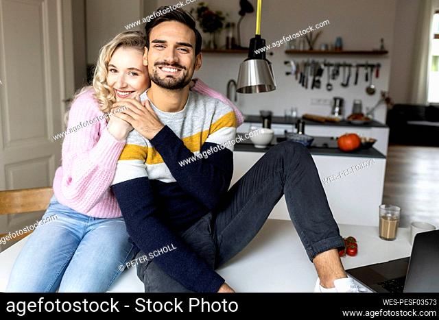 Smiling woman embracing boyfriend sitting on table at home