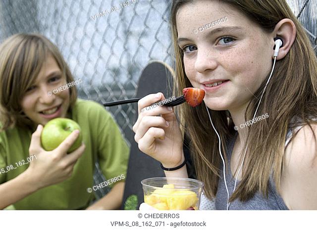 Portrait of a teenage boy holding an apple and sitting with a teenage girl eating fruit salad