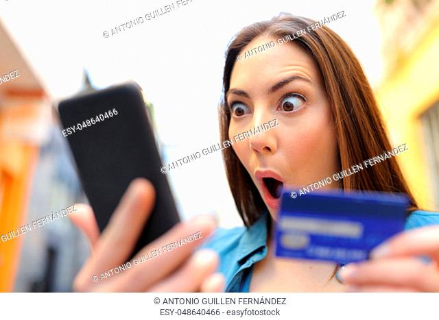 Amazed woman buying with credit card finding discount on smart phone in the street