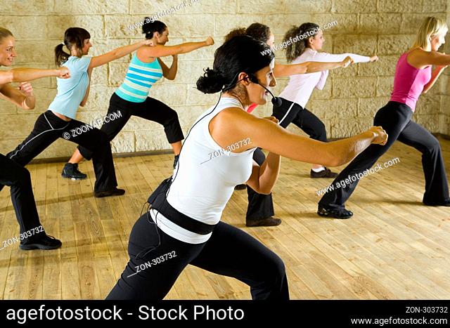 A group of women exercising with fitness instructor in the gym. Focus on the woman in white shirt. Side view
