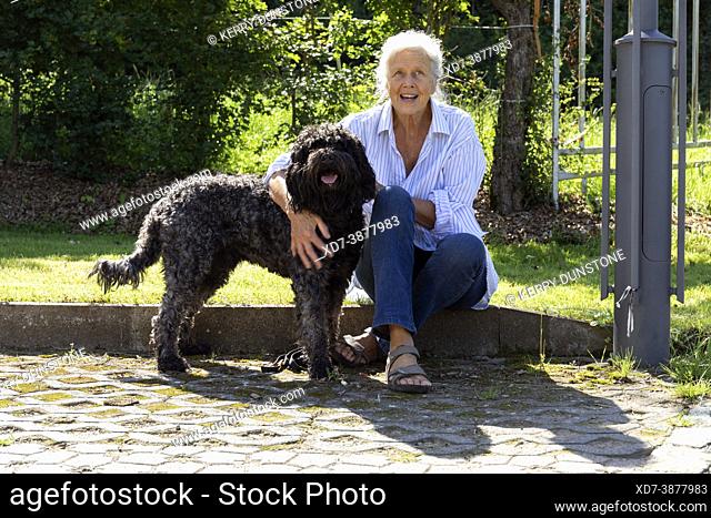Europe, Luxembourg, Septfontaines, Older woman sitting with her Pet Portuguese Water Dog