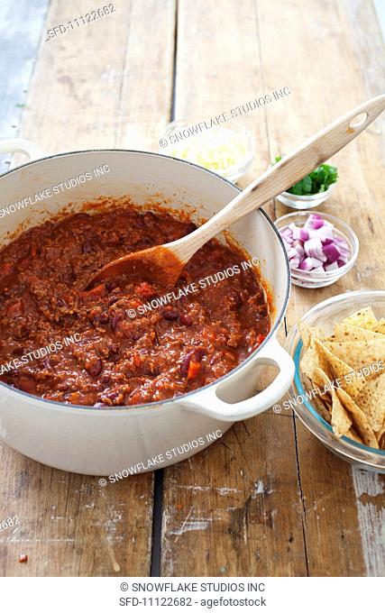Pot of Beef Chili with a Wooden Spoon, Toppings and Tortilla Chips