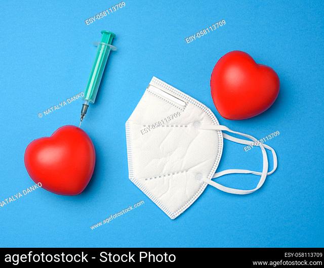 red heart and a stuck needle of a plastic syringe into it, white mask on a blue background