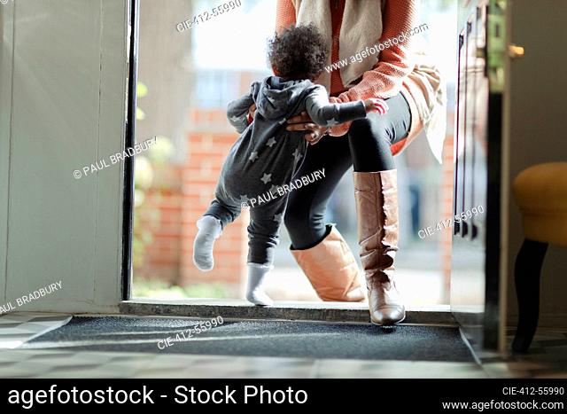 Mother lifting baby daughter in pajamas at front door