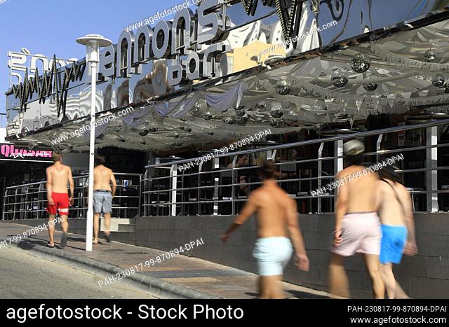 17 August 2023, Spain, Calvia: Young men walk bare-chested through Punta Ballena street in Magaluf past bars. Photo: Clara Margais/dpa