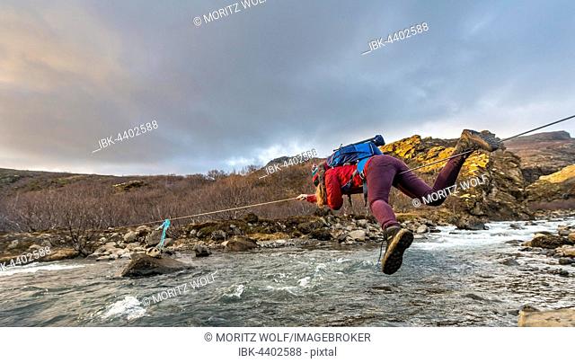 Young woman crossing river with rope, Botnsá River, Hvalfjarðarsveit, Vesturland, Iceland