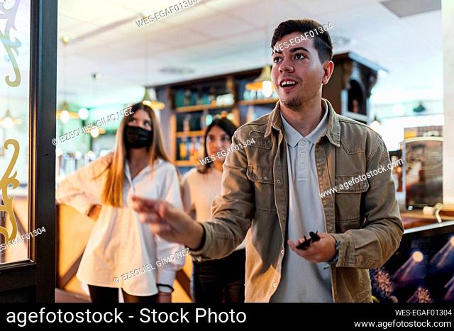 Young man playing darts with friends at bar during pandemic