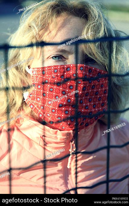Blond woman with an alternative mask behind a grid