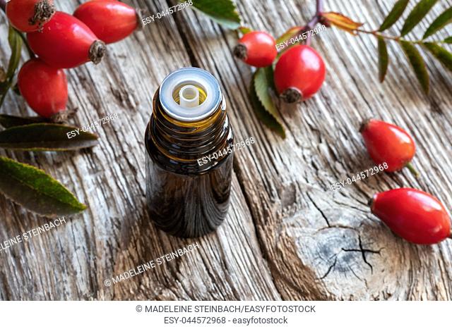 A bottle of rose hip seed oil with fresh berries and leaves