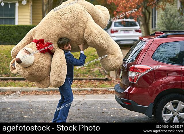 Wide shot of a man holding oversized teddy bear over his shoulder