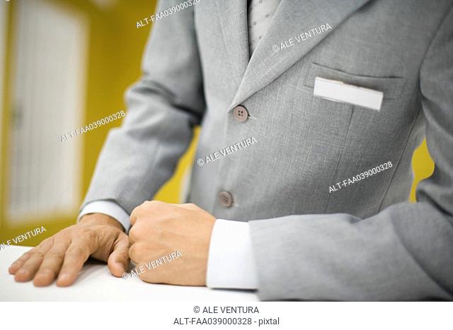 Man in suit standing behind counter, wearing blank name tag