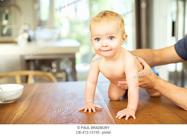 Father helping baby crawl on table