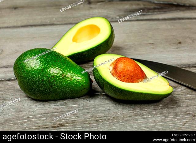 Two avocados, one cut in half, seed visible, knife next to it, on gray wood desk
