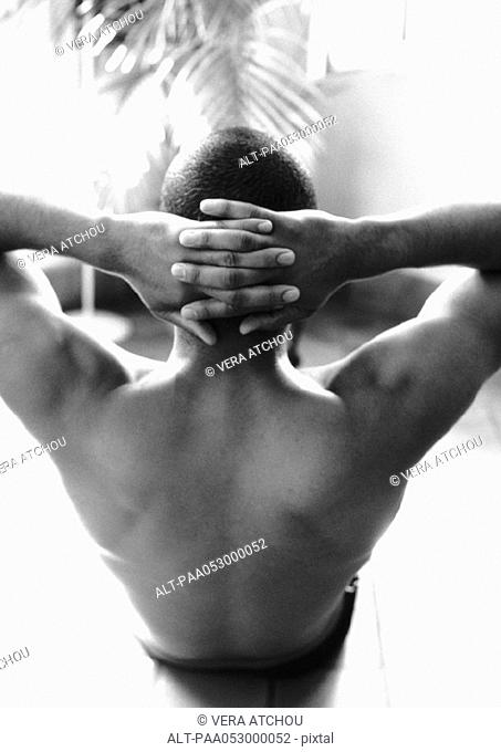 Bare-chested man doing abdominal exercises, hands behind head, rear view, b&w