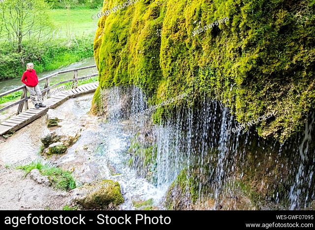 Female hiker admiring Dreimuhlen waterfall falling down mossy slope