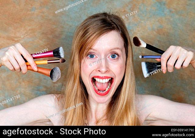 Young woman holding colorful makeup brushes and screaming with open mouth