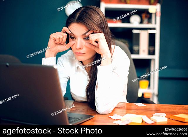 Bored lady who is about to fall asleep. Close up portrait of very tired young woman sitting in her office and trying to keep her eyes open with her hands