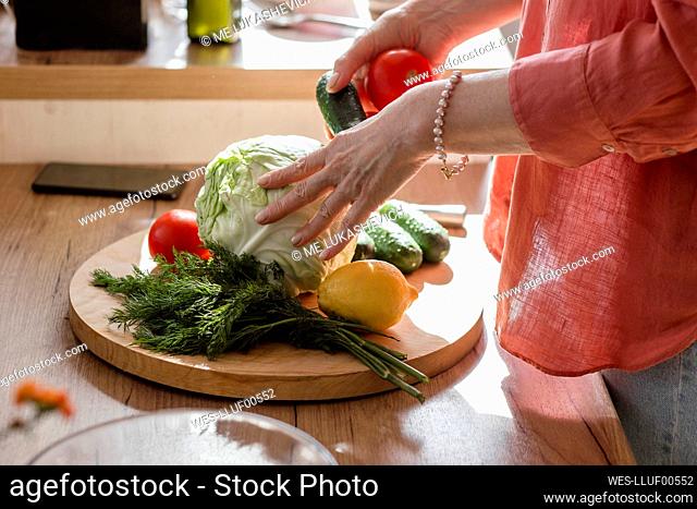 Woman sorting vegetables on wooden plate in kitchen