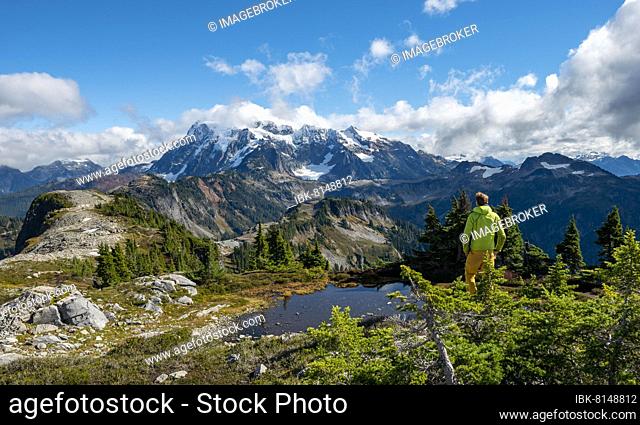 Hiker standing on a rock, Small mountain lake on Tabletop Mountain, Mt. Shuksan with snow and glacier, Mt. Baker-Snoqualmie National Forest, Washington, USA