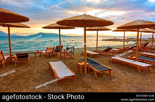 Beach with chaise-longues and straw parasols by the sea at sunset, Aegina Island, Greece. Wide angle panoramic view