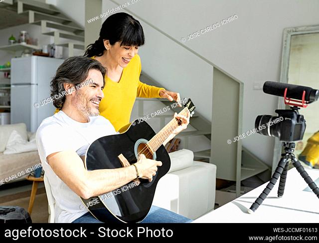 Mature couple playing guitar while vlogging through digital camera at home